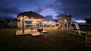 Un parque infantil con una mesa de picnic y una zona de estar cubierta al anochecer.