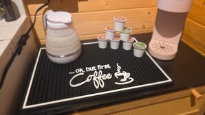 Una estació de cafè amb una cafetera Keurig, una pila de gots de cafè desposables i un cartell que diu 'OK, però primer cafè'.