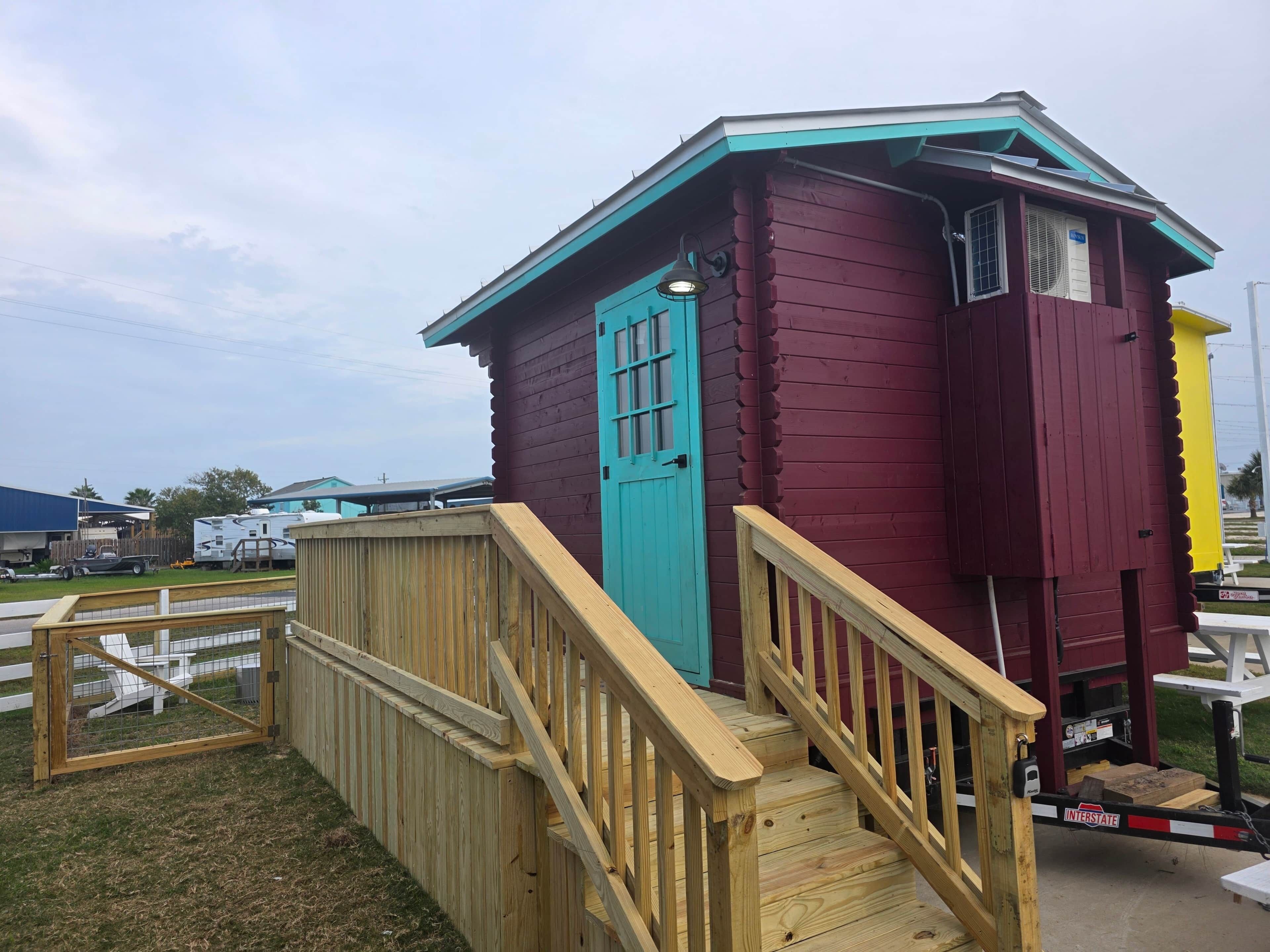 A small, single-story wooden structure with a turquoise roof and a red door.