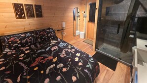 Habitació de fusta amb un llit, una dutxa i aire condicionat fixat a la paret.