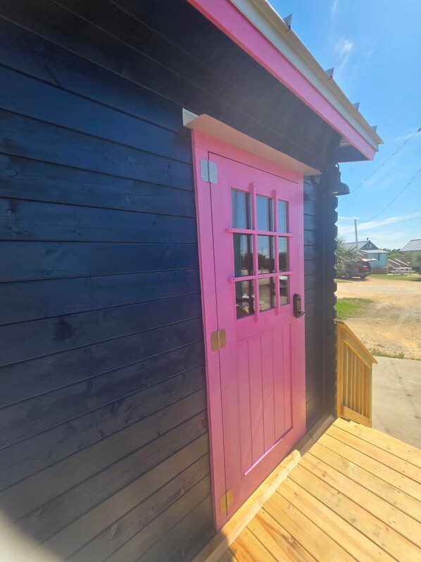 A wooden building with a pink door and a small porch.