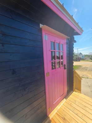 Ein Holzhaus mit einer rosafarbenen Tür und einer kleinen Veranda.