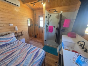Ein Zimmer in einer Holzhütte mit einem Bett, einer Dusche und einem Waschbecken.