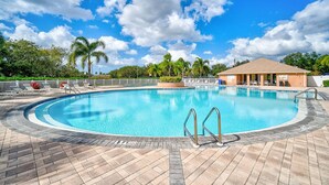 A large, clear swimming pool with a palm tree and lounge chairs around it, and a building in the background. - Peaceful Lakeside Stay with Private Screened Patio-Community Pool-Near Beaches (Bradenton)