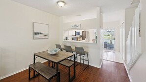 A dining area with a wooden table and chairs, a kitchen in the background, and a view of the outdoors through a glass door. - Peaceful Lakeside Stay with Private Screened Patio-Community Pool-Near Beaches (Bradenton)