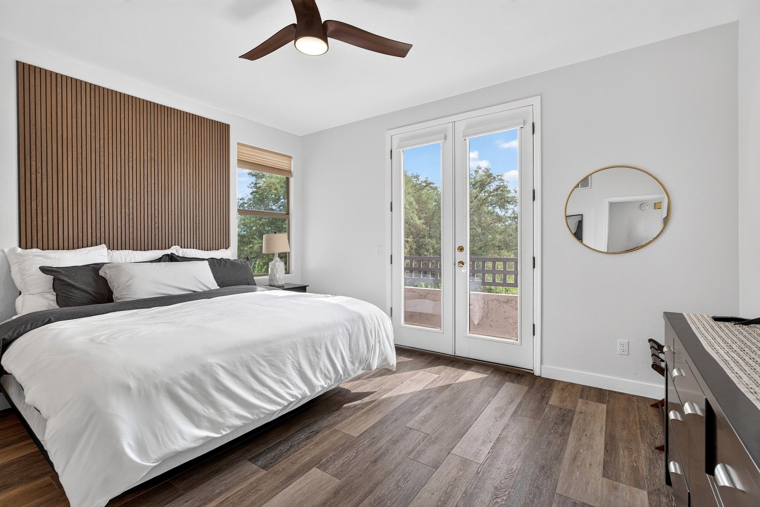 Une chambre à coucher avec un lit, un ventilateur de plafond, une fenêtre avec des stores et une vue sur l’extérieur.