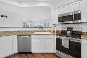 A modern kitchen with white cabinetry, a granite countertop, a dishwasher, a microwave, and an oven. - Kierland Retreat | Golf Views + Pool (Scottsdale)