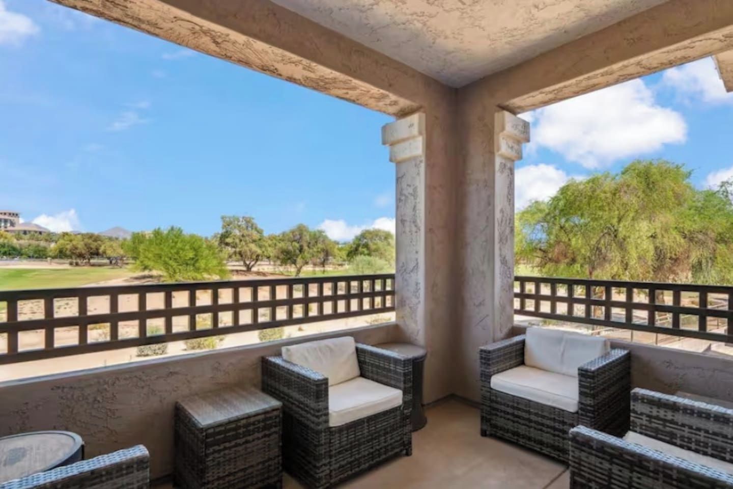 A balcony with wicker furniture and a view of a park.