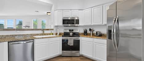 A modern kitchen with white cabinets, stainless steel appliances, and a granite countertop.