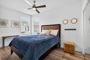 A bedroom with a bed, a ceiling fan, a window with blinds, a bedside table, and a small stool. - Kierland Retreat | Golf Views + Pool (Scottsdale)