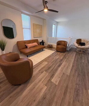 A living room with a brown leather sofa, a brown leather armchair, a wicker chair, and a ceiling fan. - Kierland Retreat | Golf Views + Pool (Scottsdale)