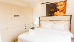 A hotel room with a large bed, a wardrobe, a nightstand, and a wall-mounted artwork. - Serene Studio Apartment at Oasis Park (Accra)