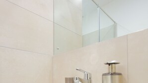 A bathroom with a white sink, a glass shower enclosure, and a mirror. - Serene Studio Apartment at Oasis Park (Accra)