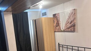 Un letto singolo con materasso e cuscini grigi, una coperta bianca, una testiera in legno e un quadro appeso al muro raffigurante un edificio.
