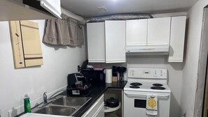 Una cucina compatta con mobili bianchi, un fornello, un forno a microonde e un lavello.