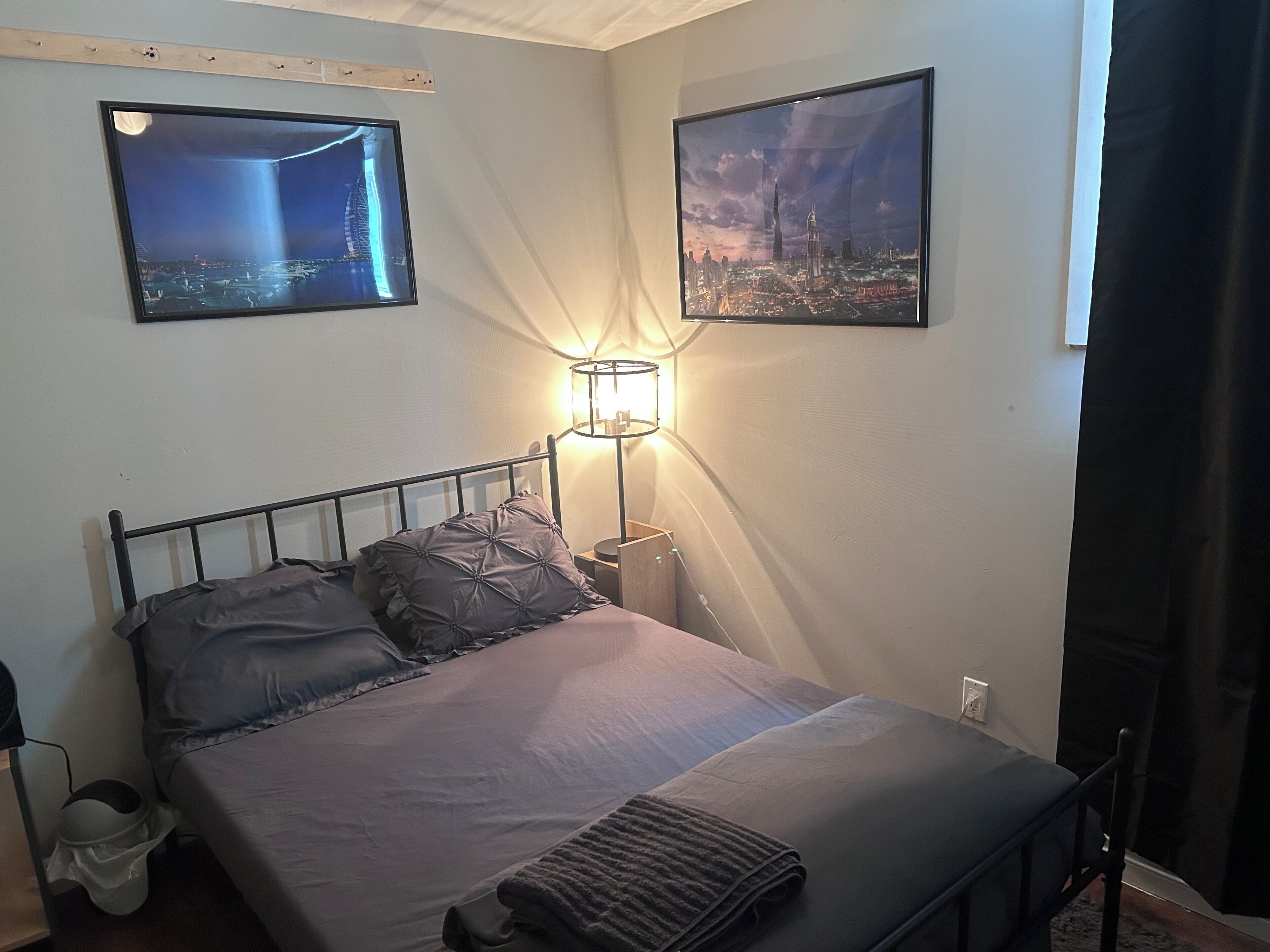 A bedroom with a bed, a nightstand, a lamp, and two framed pictures on the wall.