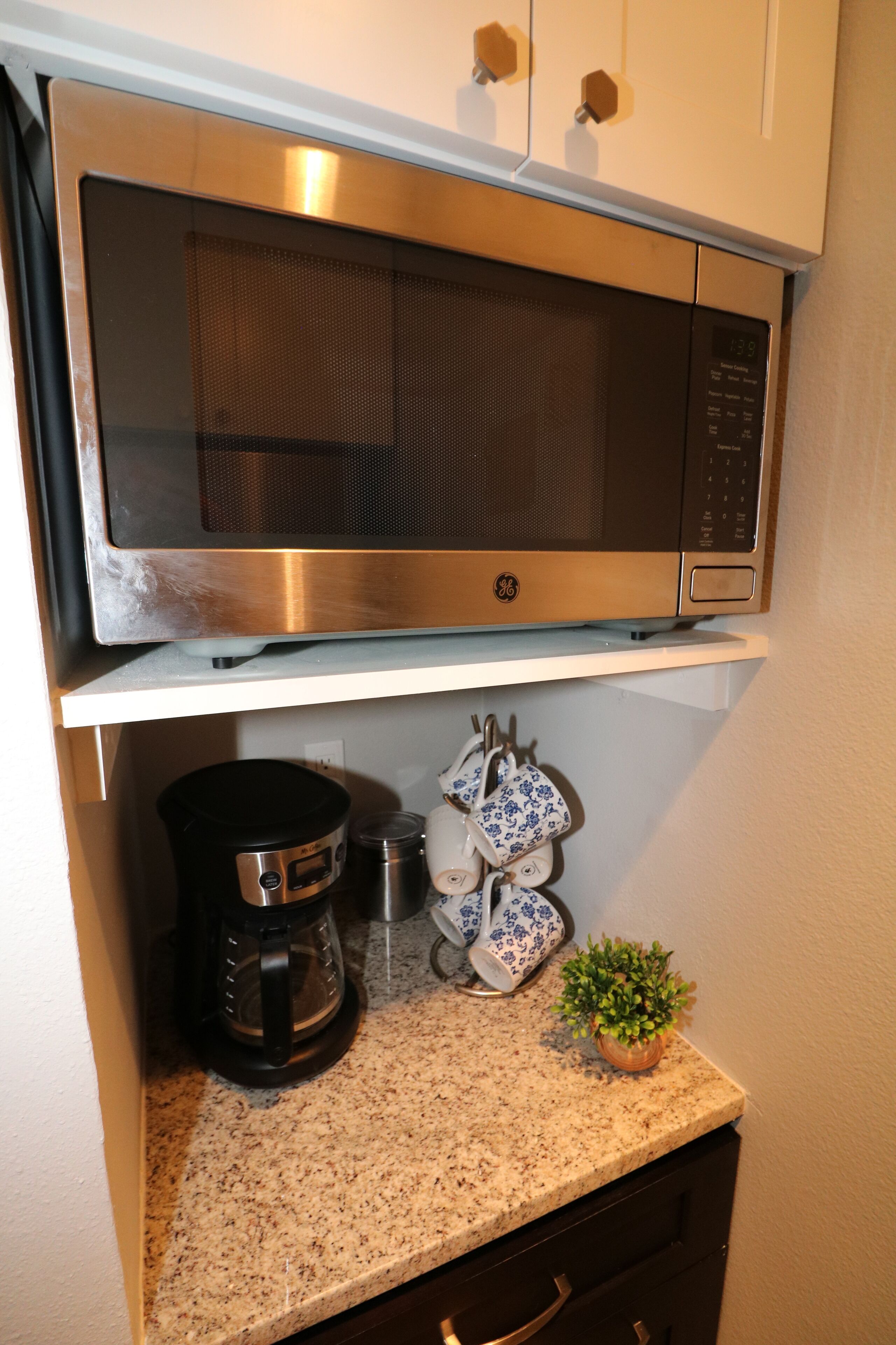 A kitchen with a stainless steel microwave, a coffee maker, and a small potted plant on the counter.