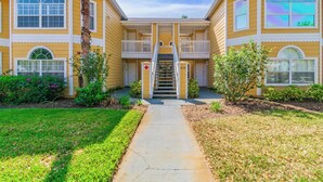 A yellow building with a central staircase, large windows, and a well-maintained lawn. - It's All NEW & Near Disney! Designer Kitchen, Sleeps 6, NO Steps, Patio, Pool (Kissimmee)
