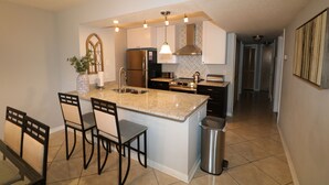 A modern kitchen with granite countertops, stainless steel appliances, and a central island with bar stools. - It's All NEW & Near Disney! Designer Kitchen, Sleeps 6, NO Steps, Patio, Pool (Kissimmee)