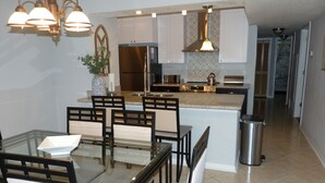 A modern kitchen with a dining area, featuring a glass table, chairs, stainless steel appliances, and pendant lighting. - It's All NEW & Near Disney! Designer Kitchen, Sleeps 6, NO Steps, Patio, Pool (Kissimmee)