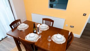 Mesa de comedor preparada para cuatro personas, con platos blancos, cubiertos y copas de vino.