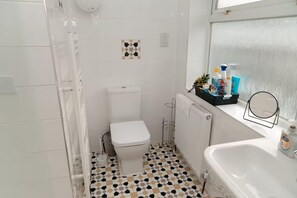 A bathroom with a toilet, a sink, and a shower area. There is a tiled floor with a geometric pattern. - House - Sleeps 5 - Ensuite Bedrooms (Camberley)