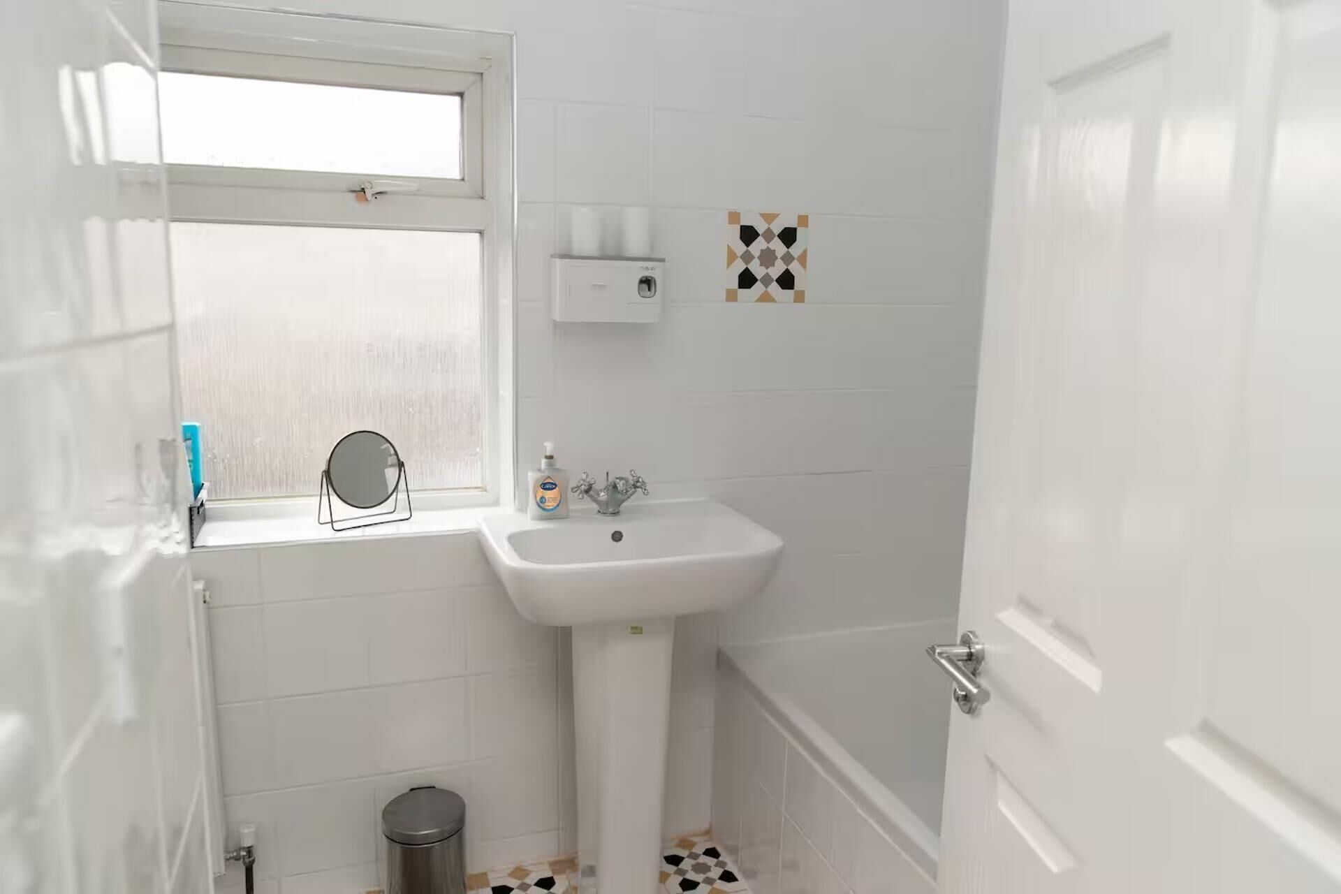 A small bathroom with a window, a sink, a mirror, and a toilet.