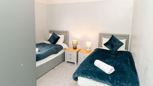 Una habitación de hotel con dos camas, cada una con cabecero, mesitas de noche y lámparas.