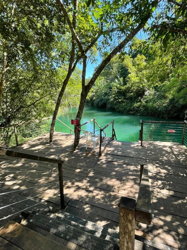 A wooden deck with a rope barrier, a bench, and a view of a calm river surrounded by dense greenery. - Camping Rio Formoso LTDA (Bonito)