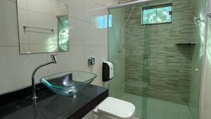 A modern bathroom with a glass sink, a toilet, a shower, and a mirror.