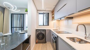 A modern kitchen with a built-in washer and dryer, a dining area with a table and chairs, and a large window providing natural light. - Fully Equipped Apartments in a Building With a Pool, 400m From Picarras Beach - Bacs (Picarras)