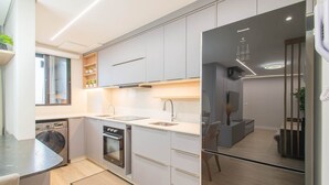 A modern kitchen with built-in appliances, a dining area with a TV, and a separate living space with a sofa and a plant. - Fully Equipped Apartments in a Building With a Pool, 400m From Picarras Beach - Bacs (Picarras)