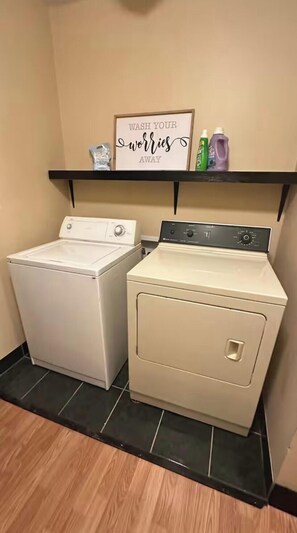 A laundry area with two washing machines, a shelf with cleaning supplies, and a sign that says 'WASH YOUR WORRIES AWAY.' - Spacious Indy Home Near Downtown. Book 5 Nights, get 1 free (Indianapolis)