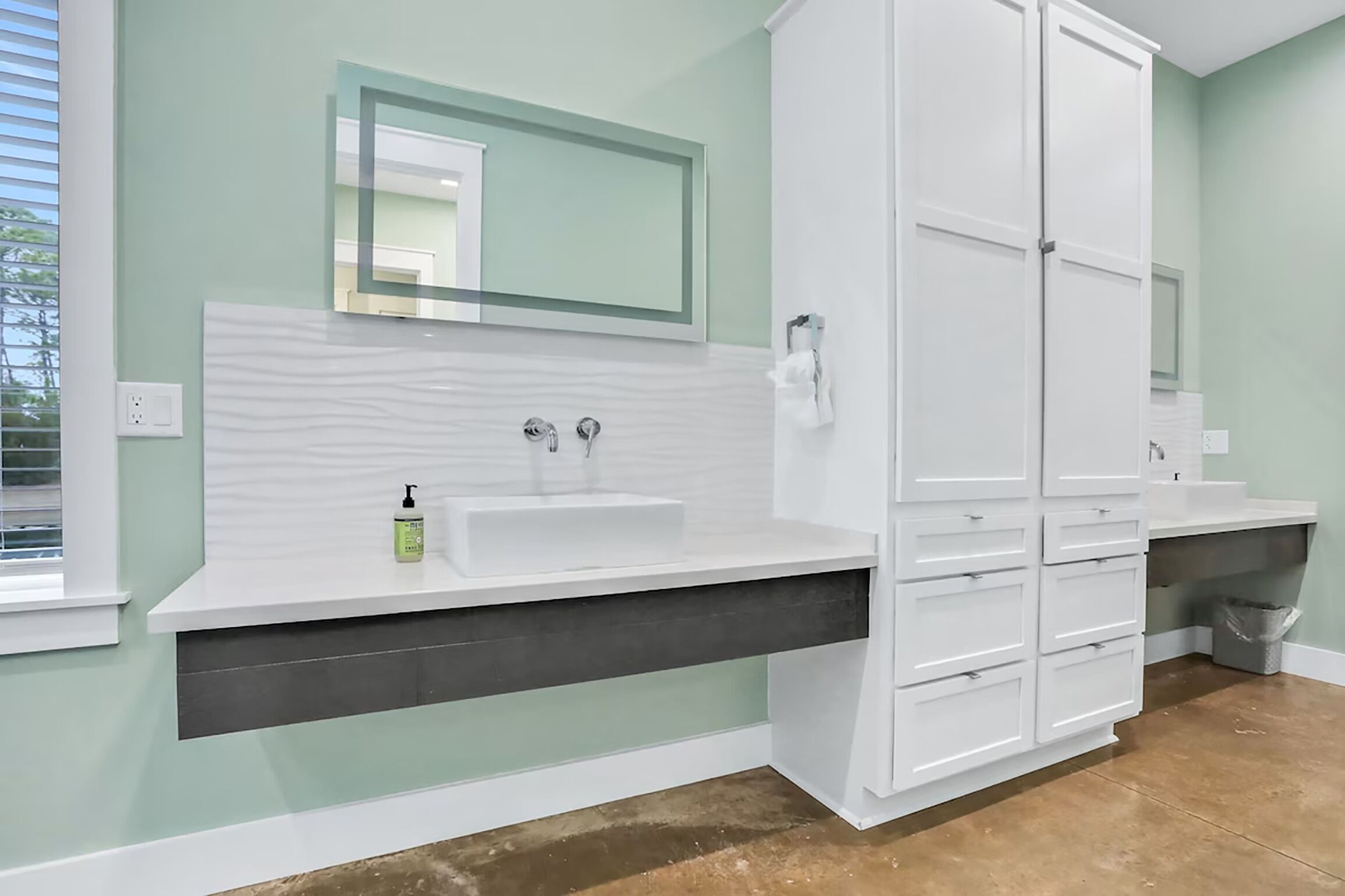 A bathroom with a white vanity, a large mirror, and a white cabinet.