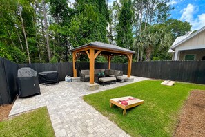 A backyard with a wooden gazebo, outdoor seating, a grill, and a small table. - Down da Road (Miramar Beach)