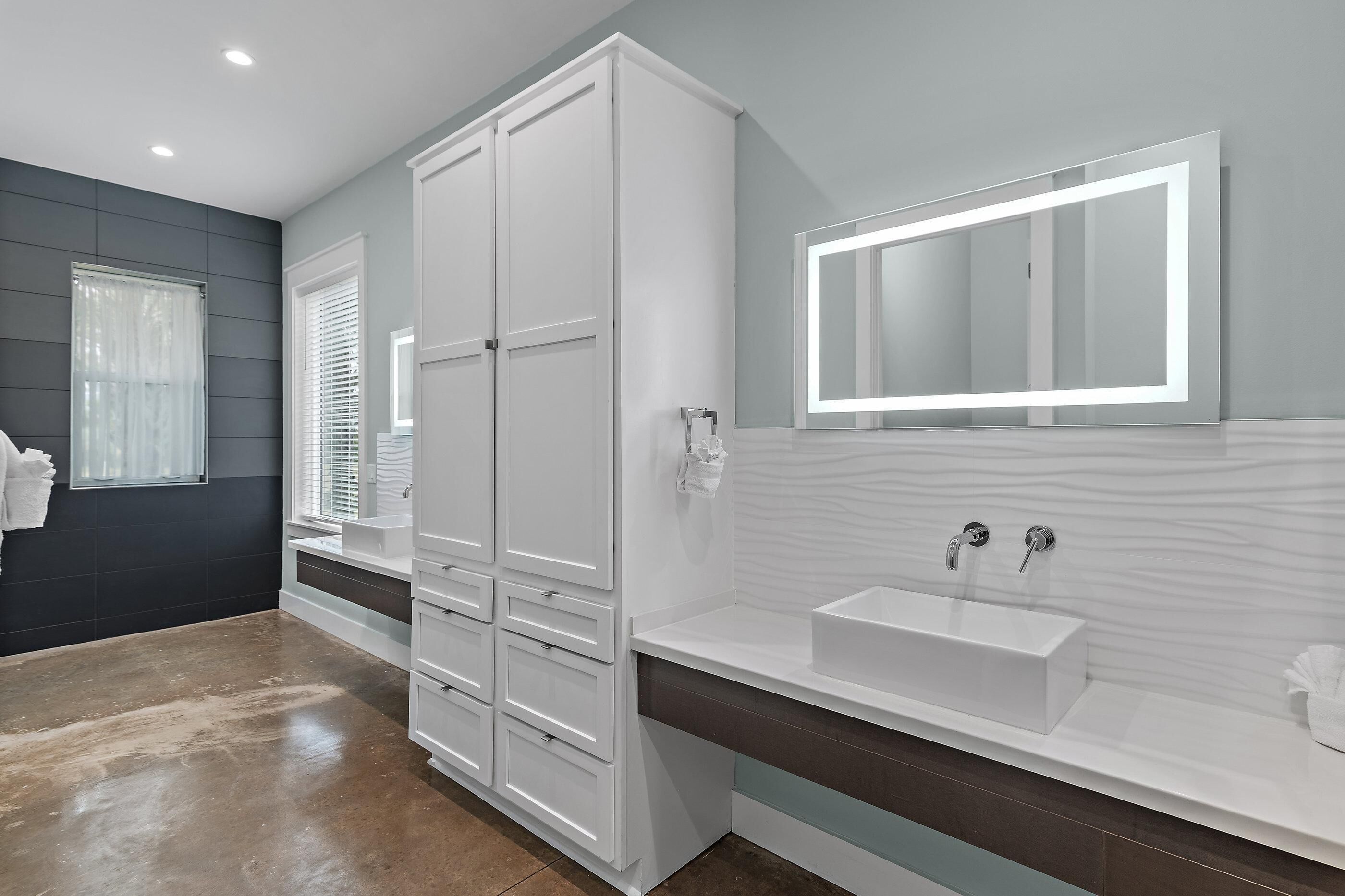 Une salle de bain moderne avec un grand miroir, des meubles blancs et un lavabo rectangulaire.
