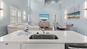 Una cocina moderna con una isla central, un comedor con mesa y sillas de madera, y una sala de estar con sofá y televisor.