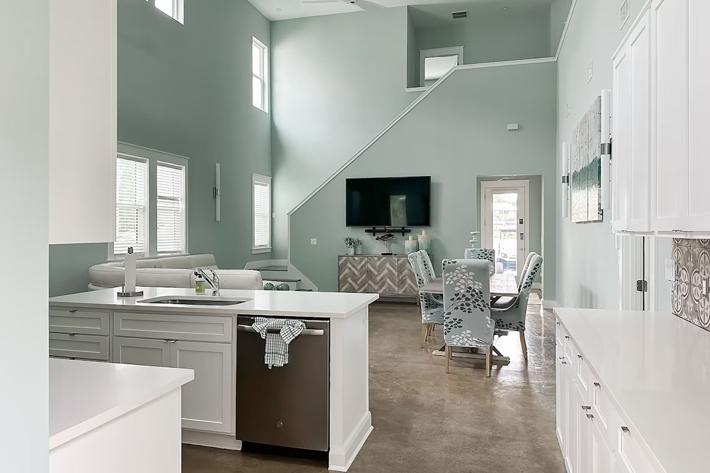 A spacious kitchen with a central island, a dining area with patterned chairs, and a staircase leading to an upper level.