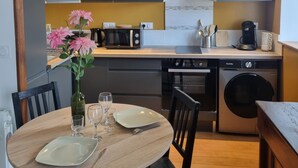 Eine moderne Küche mit Edelstahlgeräten, ein Essbereich mit einem Holztisch und Stühlen sowie eine Vase mit Blumen auf dem Tisch.