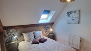 Ein Schlafzimmer mit Dachfenster, einem Bett mit gemusterten Betttextilien, einer Nachttischlampe und einer Heizung.