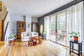 Uma sala de estar espaçosa com piso de madeira, um sofá branco, uma mesa de centro redonda e um espaço de jantar com mesa e cadeiras.