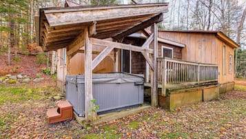 A rustic wooden cabin with a hot tub, a wooden deck, and a fenced area.