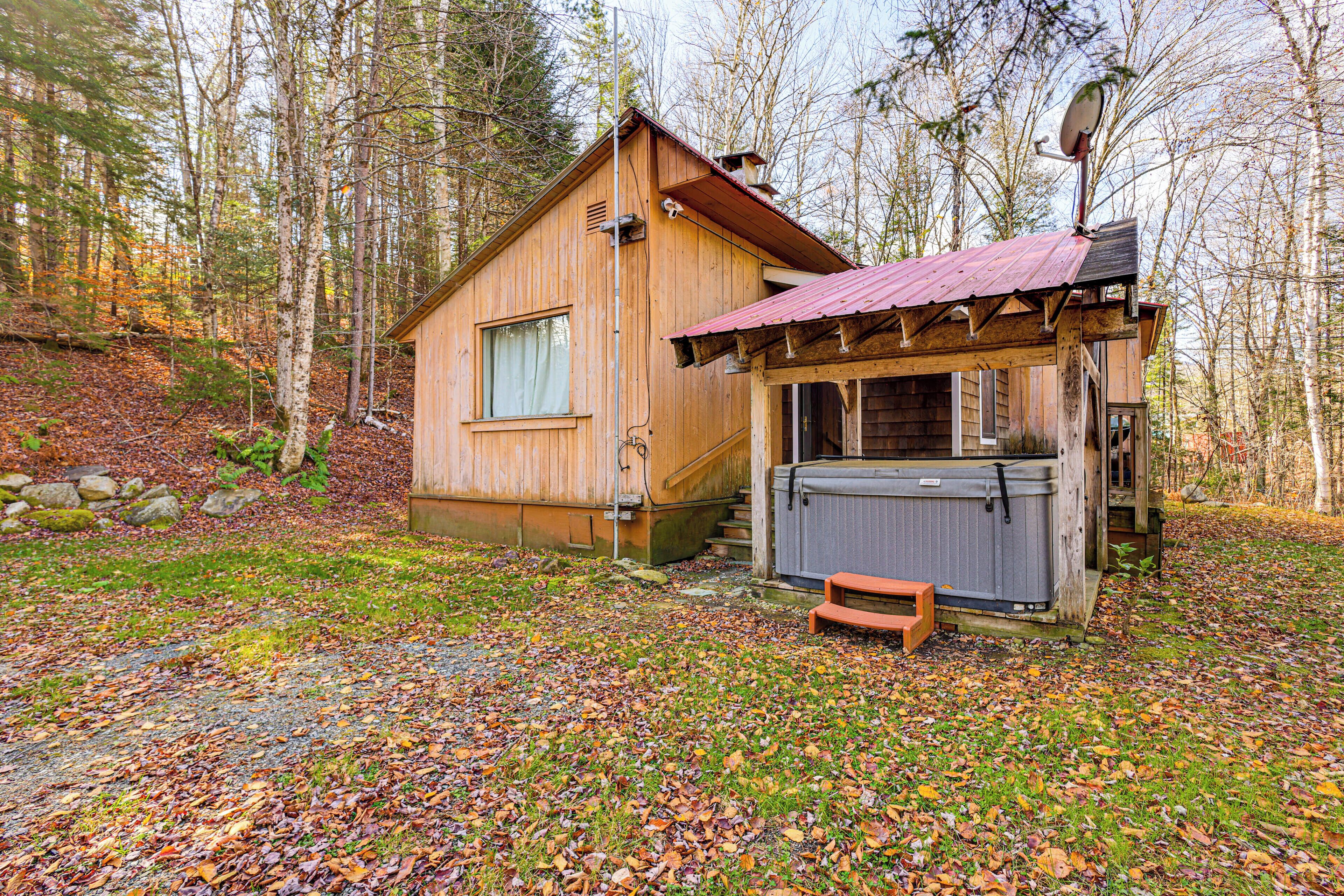 A wooden cabin with a metal roof, a hot tub, and a bench in a forested area.
