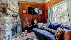 Een gezellige woonkamer met een stenen openhaard, een blauwe bank en een groot raam met gordijnen.