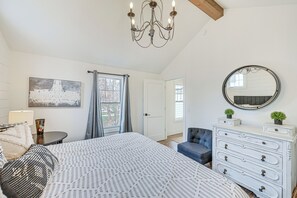 Une chambre à coucher avec un grand lit, une commode, une chaise, un lustre, un miroir et une fenêtre avec des rideaux.
