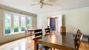 A spacious dining area with a large wooden table, several chairs, a ceiling fan, and large windows offering a view of greenery outside. - Serene & Spacious! Family-Friendly Catharpin Home (Catharpin)