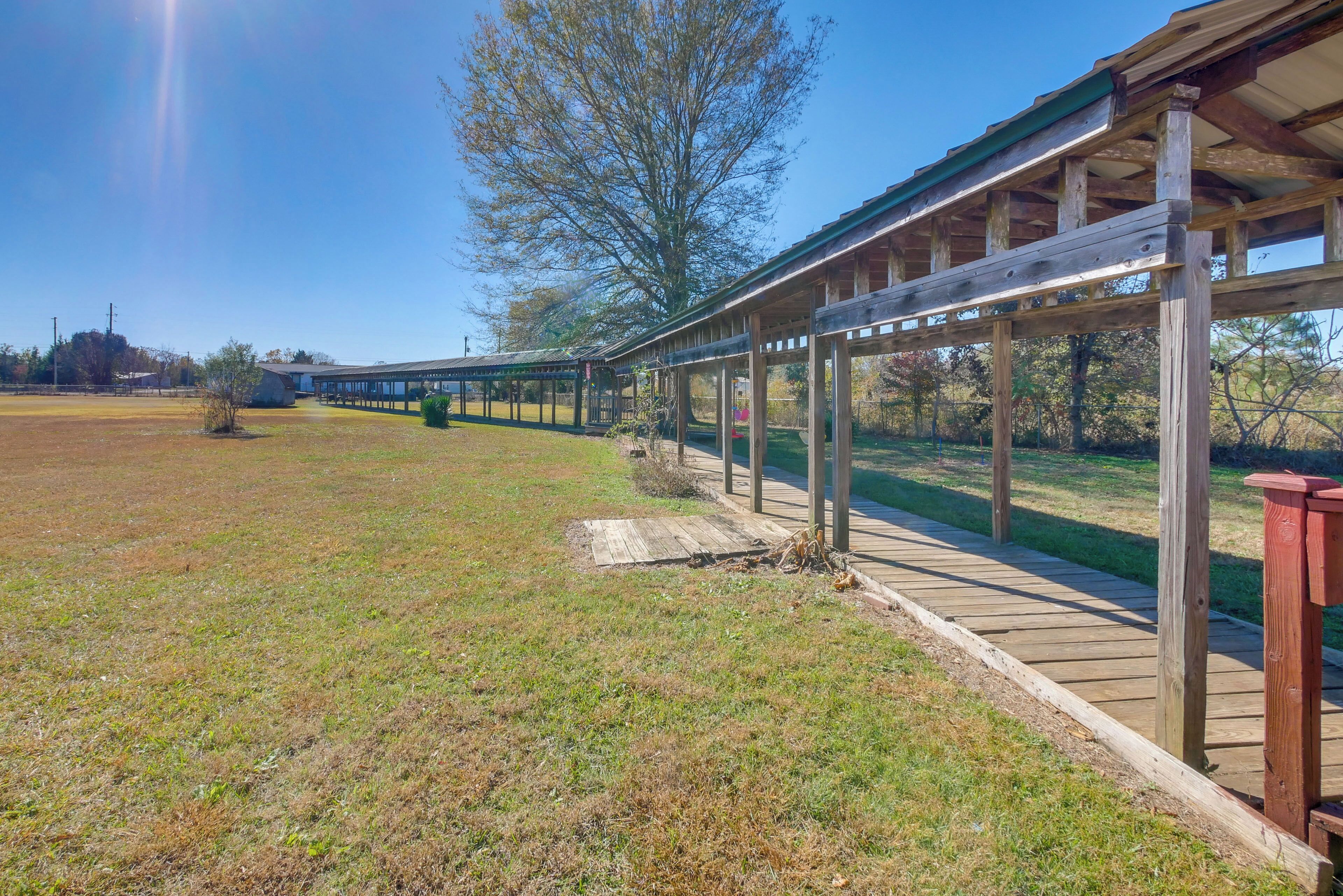 A covered wooden walkway with a metal roof, surrounded by grassy fields and trees.
