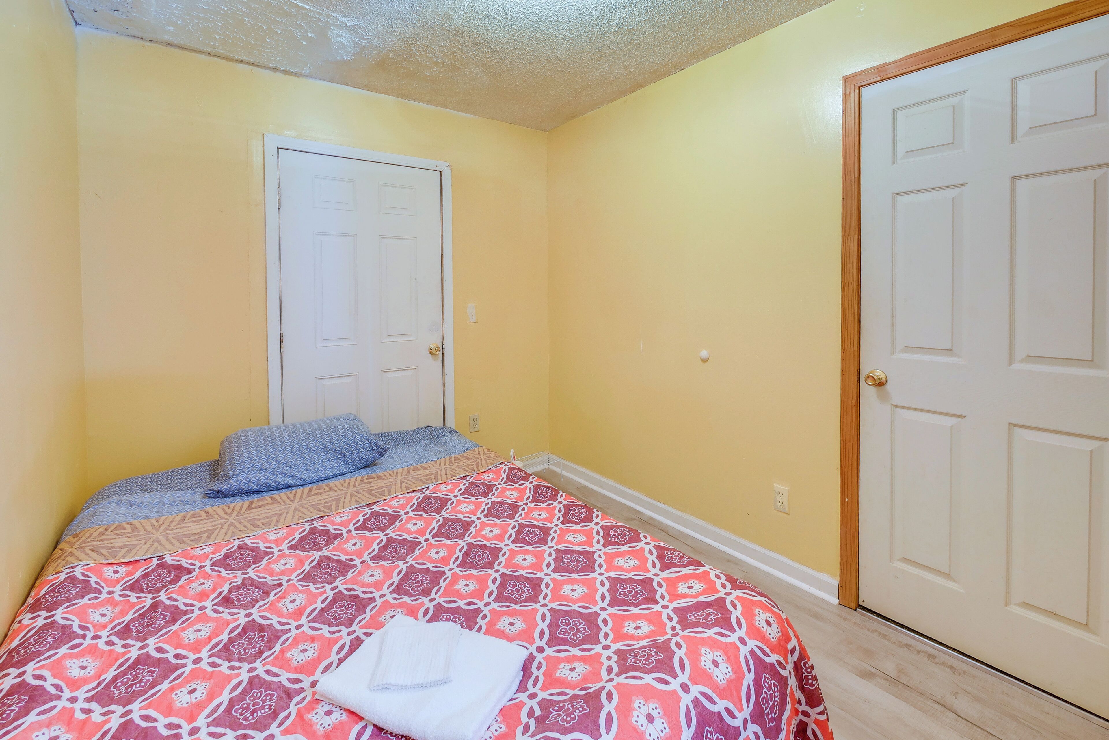 A bedroom with a bed, two doors, and a plain wall.