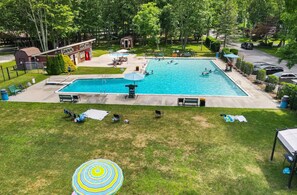 A rectangular swimming pool with a surrounding deck, benches, and umbrellas. - 5BR Poconos Cabin Near Jim Thorpe, Sleeps 10 (Jim Thorpe)