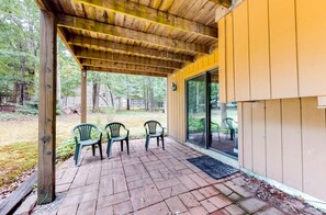 A covered patio with brick flooring, two green plastic chairs, and a glass door leading to an outdoor area. - 5BR Poconos Cabin Near Jim Thorpe, Sleeps 10 (Jim Thorpe)